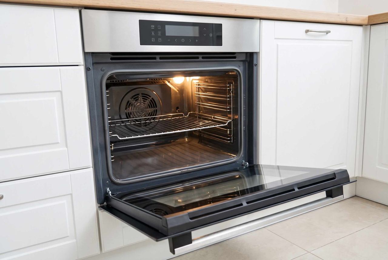 A built-in oven in a white kitchen, door open and interior spotless after a professional oven clean