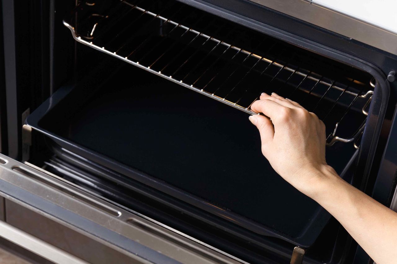 Sliding a clean oven shelf back into place after a deep clean in an Arundel kitchen