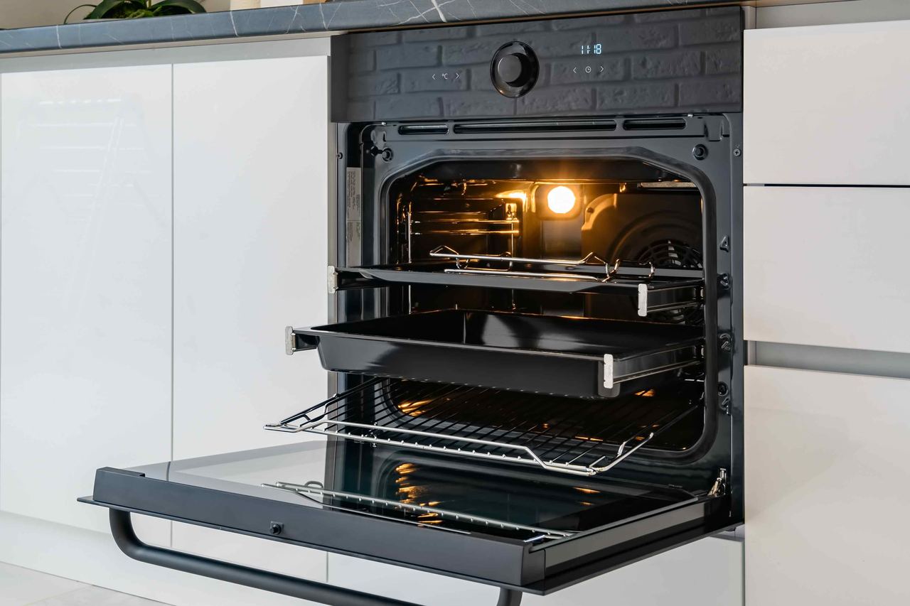 A spotless single oven with its door open in a bright Chichester kitchen, marble splashback and pans on the hob above